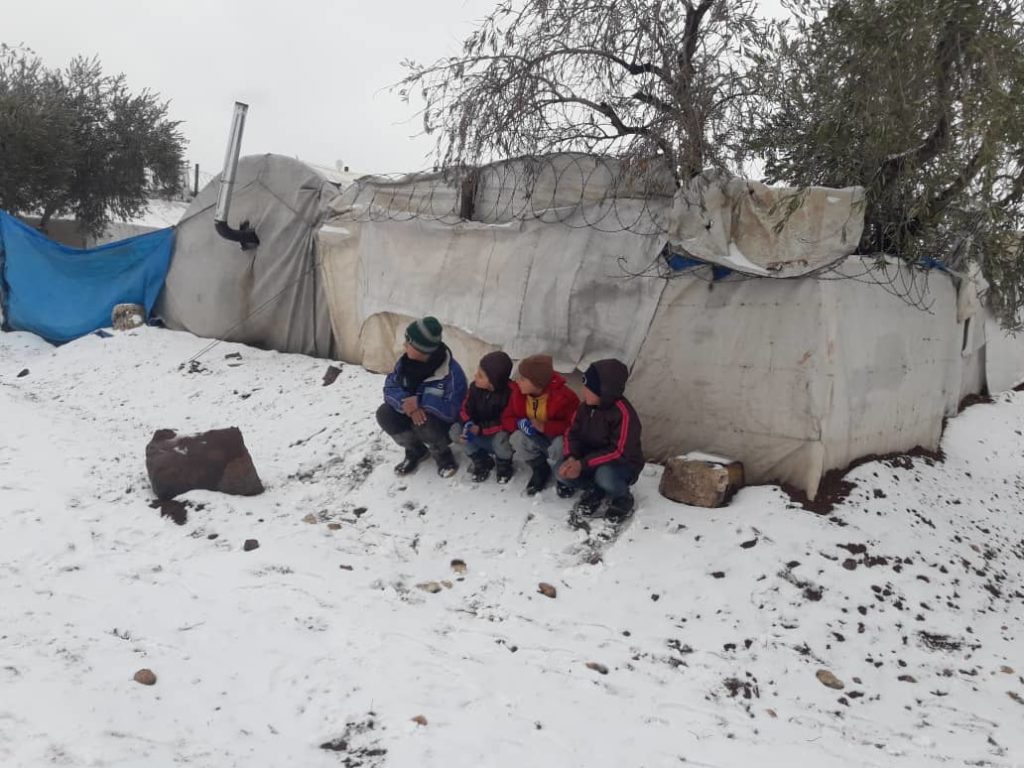 Child refugees sit in the snow.
