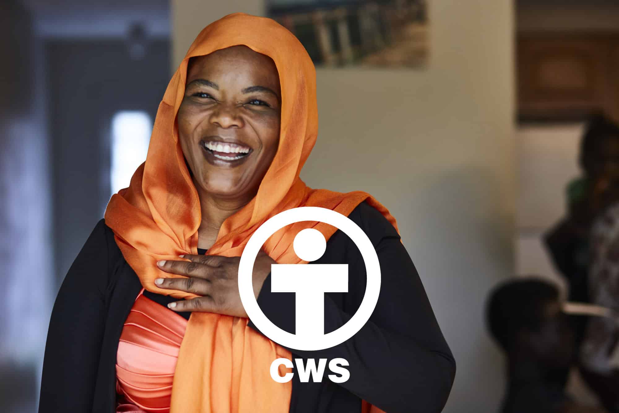 A woman in an orange head scarf smiles at the camera.