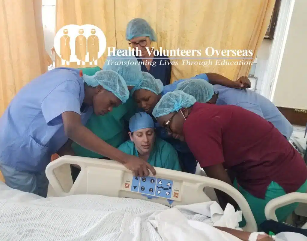 Health Volunteers Overseas logo over photo of medical professions grouped around a medical bed