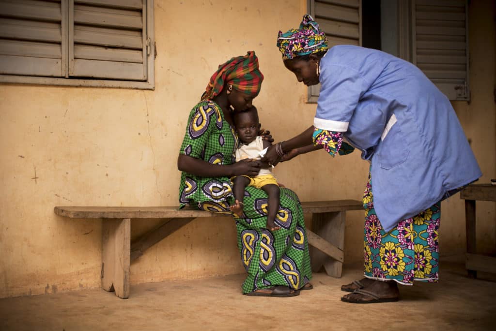 A woman holding her child while they are tested for malnutrition by another woman.