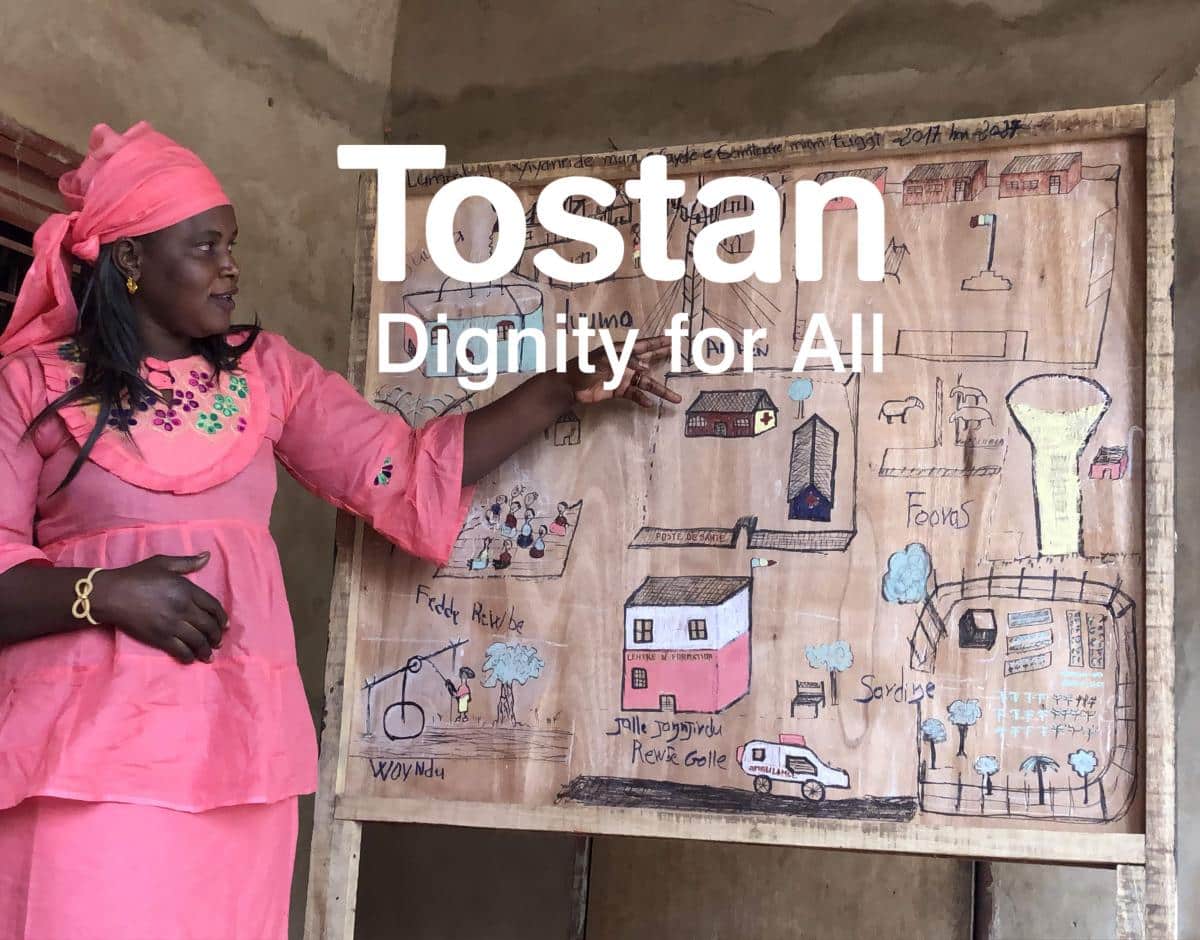 Tostan logo over photo of a woman pointing to a display board