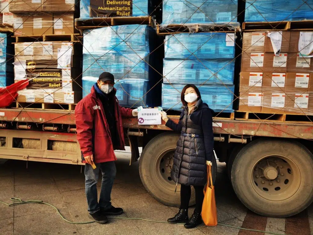 Two people stand in front of a truck loaded with pallets of supplies.