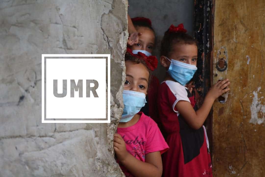 Three children peer around a corner wearing masks. White UMR logo.