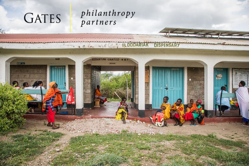 A group of people wait outside of a clinic. Gates Philanthropy Partners logo.