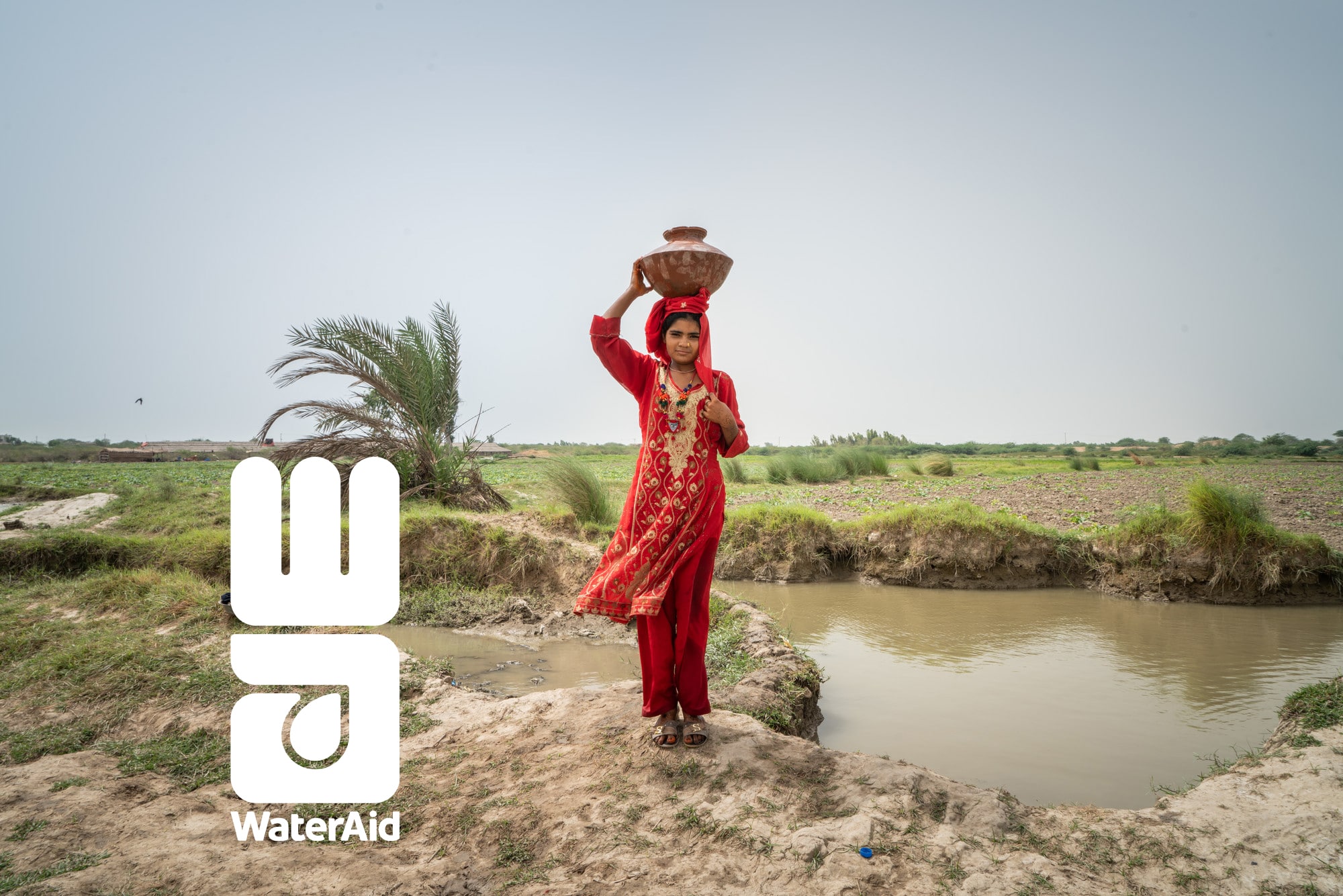 A woman carrying a pot of water on her head. WaterAid logo.