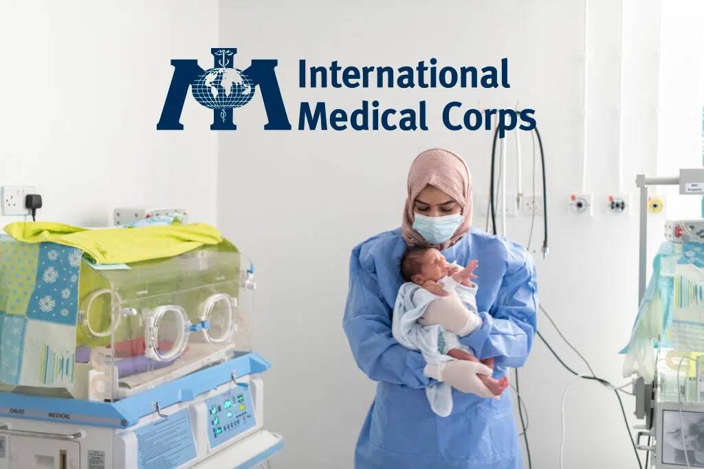 A health care worker holds a newborn baby. Logo: International Medical Corps