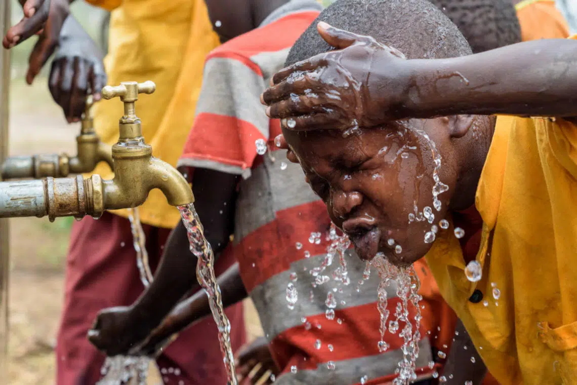 Child using World Vision's water pump to splash their face