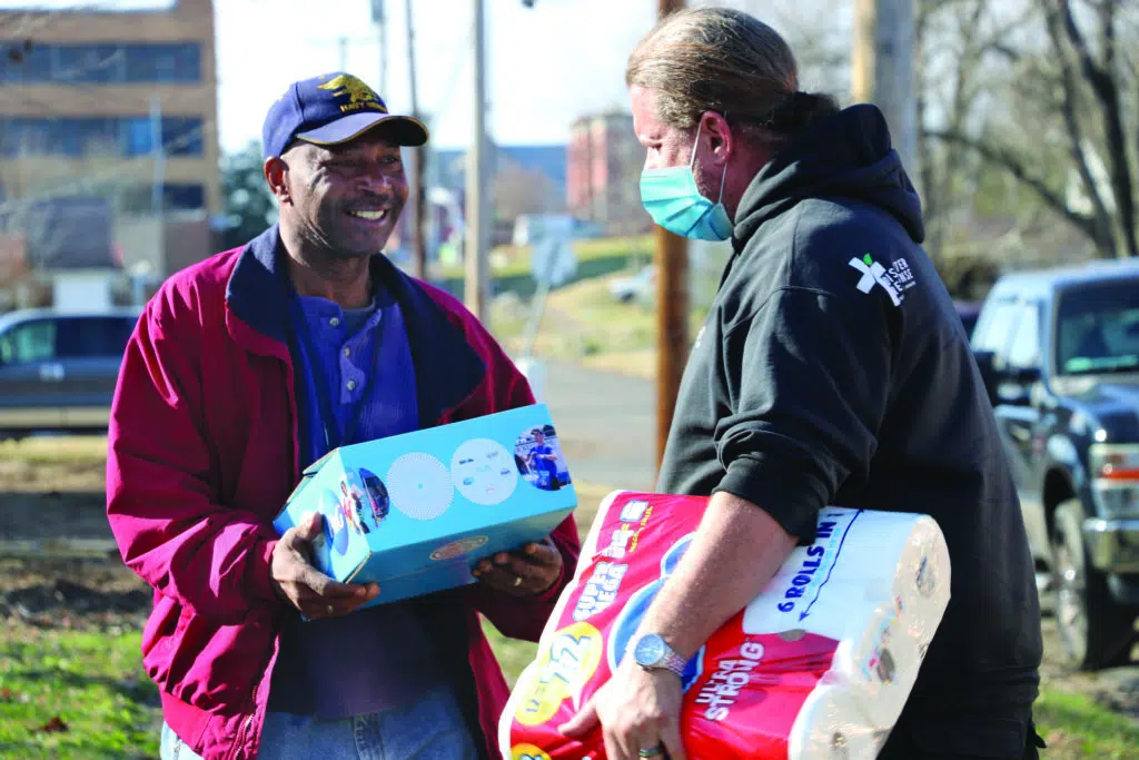 A black man receiving items from a white charity worker