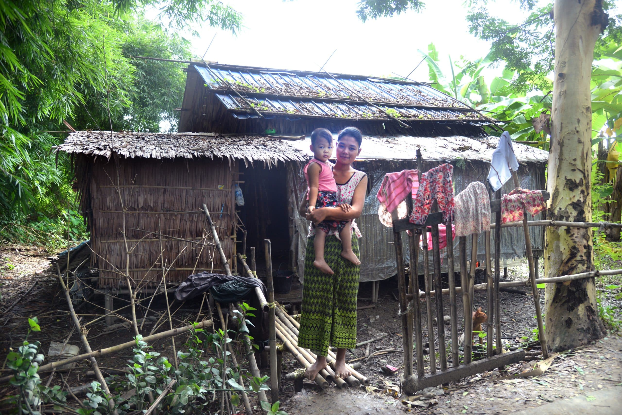 A mother holding her toddler child in front of her home in Myanmar