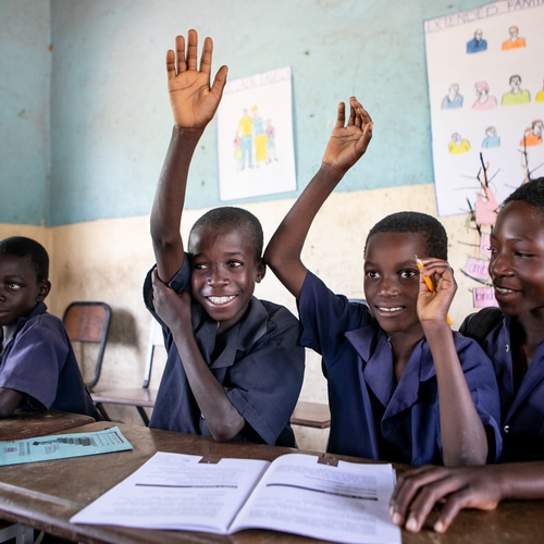 4 black schoolchildren enjoying their school work and two of them are raising their hands