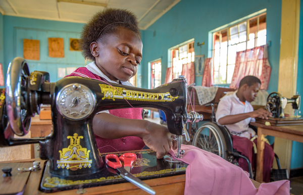 Judith Alwang, 16, learns to sew at the Nyabondo Rehabilitation Center in Katito, Kenya. This center provides education and vocational training to children and youth with disabilities. Through a USAID-funded and World Vision-implemented program, Judith was one of the young people who received a wheelchair and learned about its maintenance. It's given her a freedom she never knew before. “Right now, I can do things that I was not able to do before, so my life has transformed,” Judith says. “I think that my future will be bright.” Summary: Judith Ajwang, 16, was brought to the Nyabondo Rehabilitation Center in Katito, Kenya by her aunt. Her parents died when she was young; she has no memory of them. “My auntie didn’t love me, and she didn’t welcome me,” says Judith. But her aunt did bring her to the center. Before, Judith had to crawl if she wanted to move anywhere. “I was not able to go anywhere. I was just there,” she says. Judith admired other children when they went by on their way to school, but school wasn’t an option for her. Things began to change when she arrived at the center six years ago and received sewing training. She began to be treated differently. “[The center] welcomed me very well, and I felt like I’d gotten my parents again,” Judith says. Then two years ago, she received a wheelchair through the as USAID-funded, World Vision-implemented program called ACCESS. That stands for Accelerating Core Competencies for Effective Wheelchair Service and Support. “That day, I was very happy when I received the wheelchair because I was now able to move very freely,” Judith says. She also received training on how to take care of her wheelchair and how to clean it. If something breaks, then she gets help repairing it. “Before I got the wheelchair and I was just at home, I was seeing no future,” Judith says. “I was just there, and there was nothing.” Now, when she finishes her studies, she’ll get