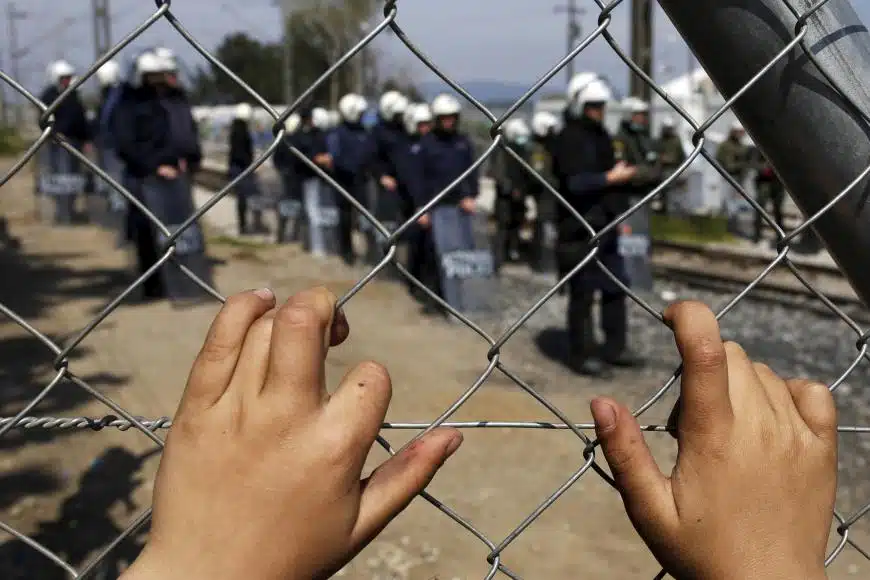 hand on a fence with police in the background