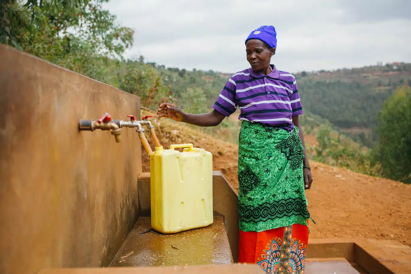 A woman in Rwanda stands next to community tap stand