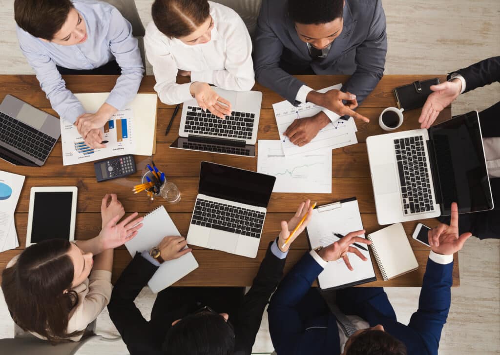 A team over a desk crowded with laptops and papers