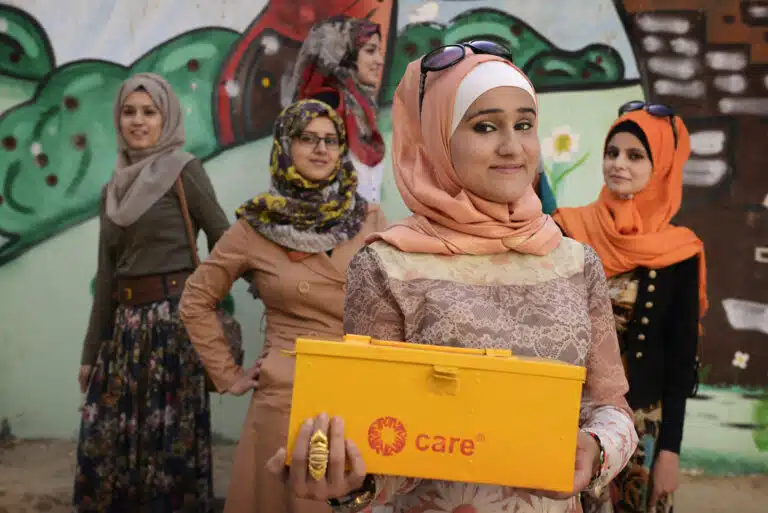 A girl holding a CARE box, with other women posing behind her