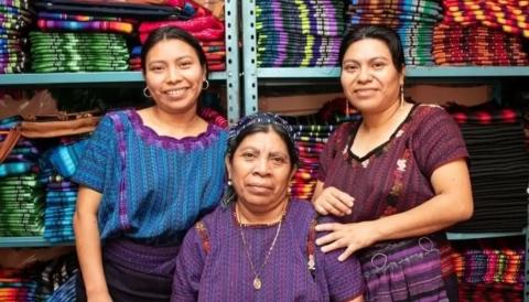 Three women posing in front of woven items