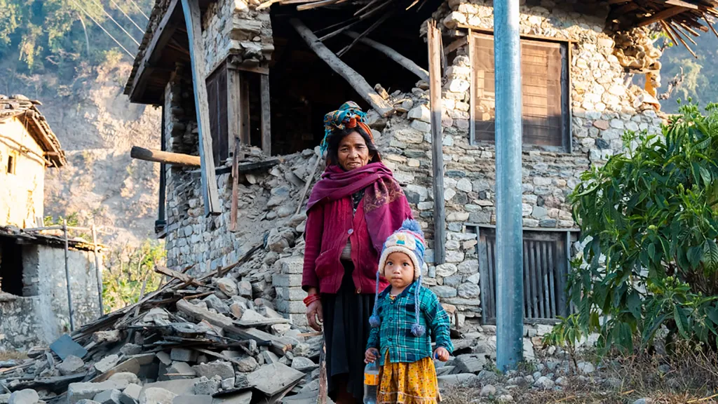 A woman and child standing in front of a destroyed house.